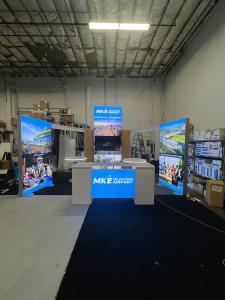 RENTAL: Modified RE-9096 Island Design with 5 ft Wide x 12 ft High Double-Sided Lightbox, (2) 4 ft Wide x 8 ft High Double-Sided Lightboxes, (2) Curved Extrusion Bridged Headers, Shortened for Smaller Booth Space, (1) Large Monitor Mount, RE-1587 Receptio